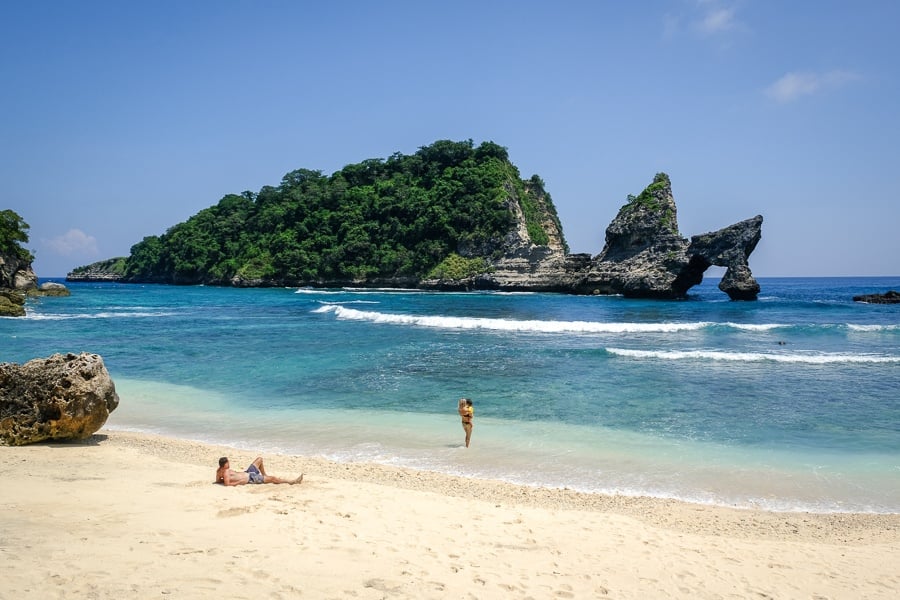 Tourist couple relaxing with their kid on the sand at Atuh Beach in Nusa Penida, Bali