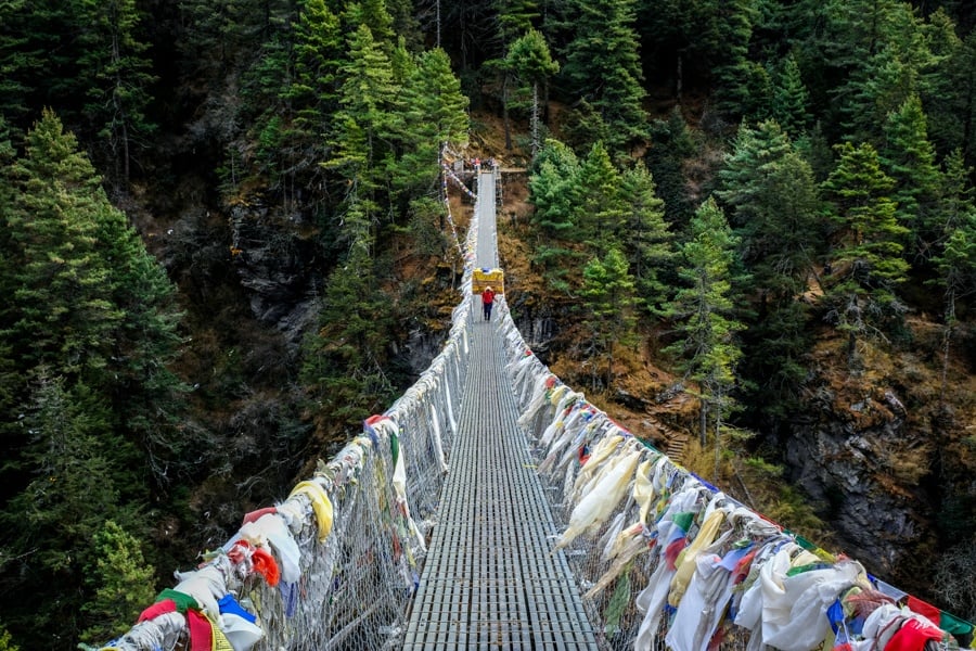Porter walking on a steep mountain bridge on the EBC trek in Nepal