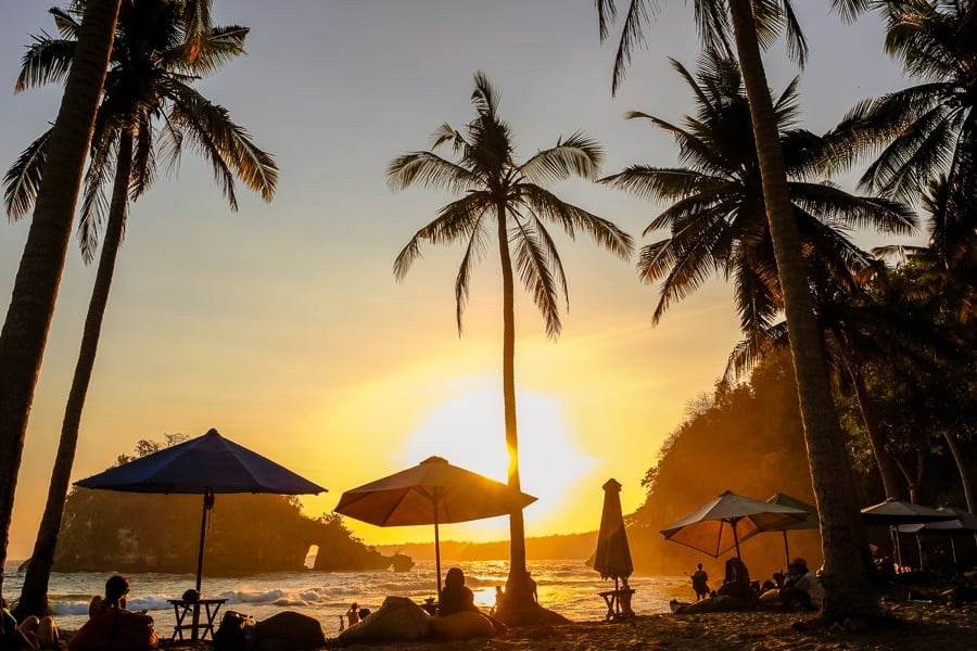 Tourists with the sunset and palm trees at Crystal Bay in Nusa Penida, Bali